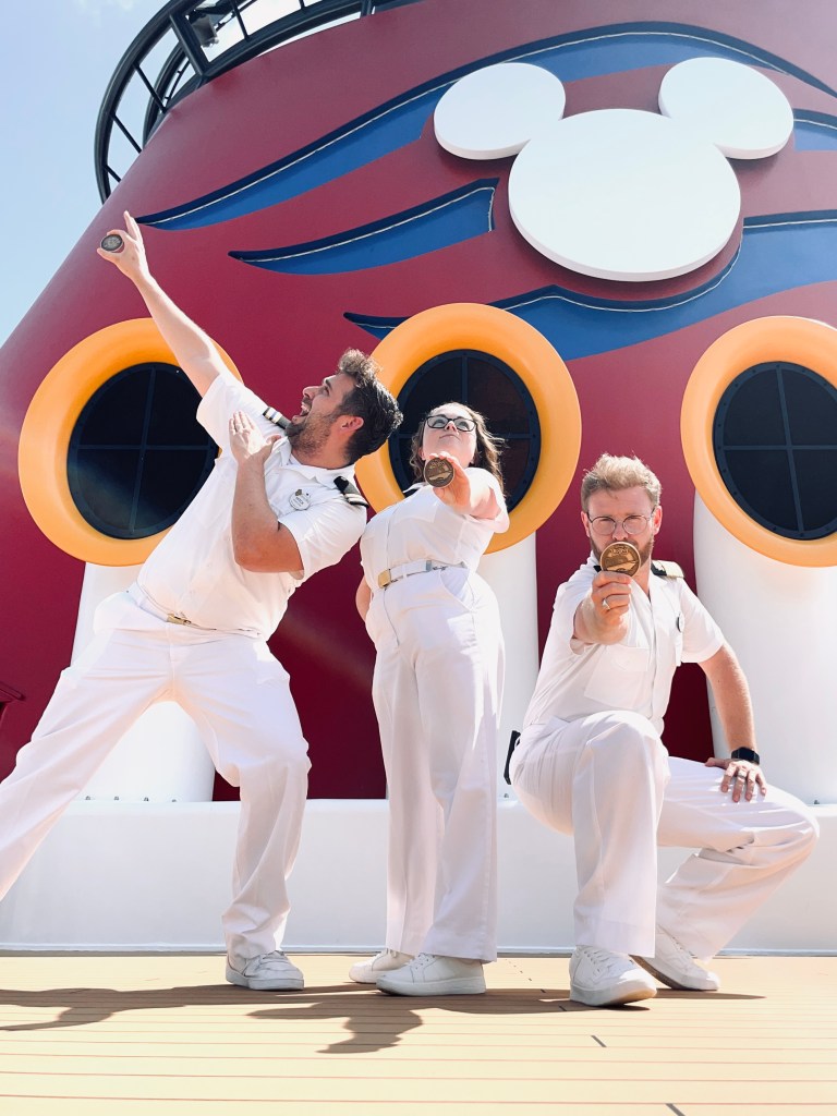 Three disney cruise line officers posing like super heros in front of mickey funnel