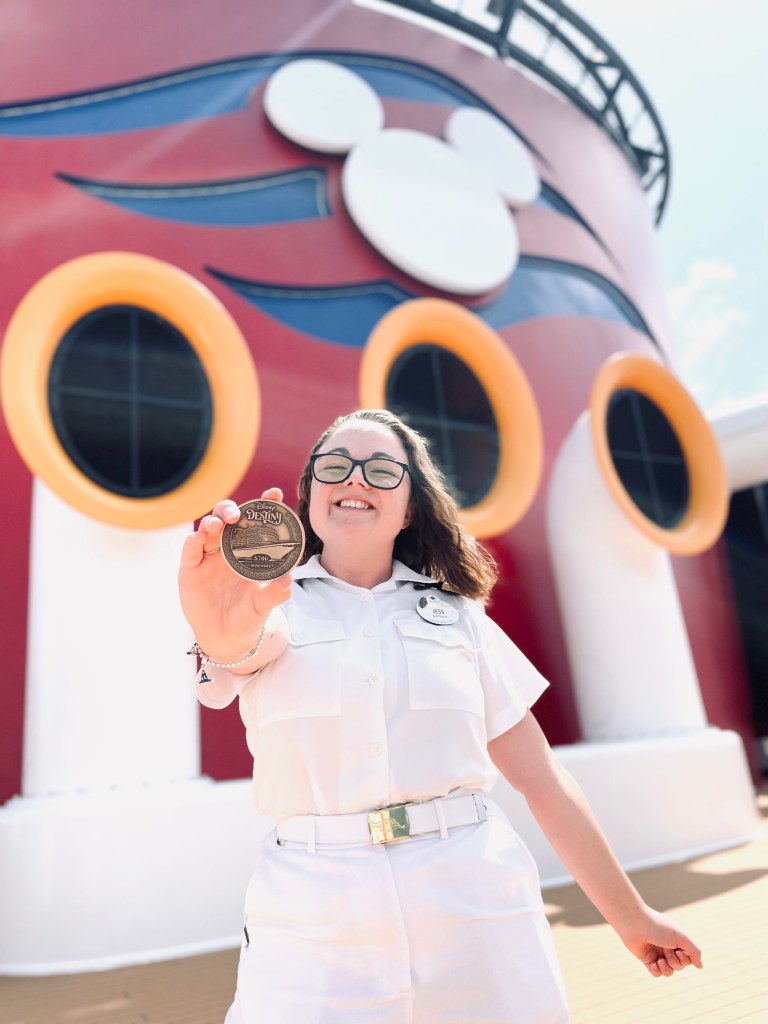 Disney cruise line officer smiling while holding a disney destiny keel coin