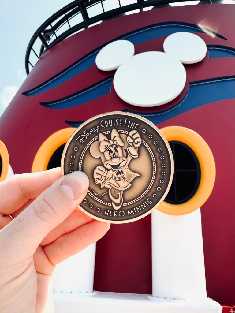 Hand holding a disney destiny keel coin in front of mickey funnel