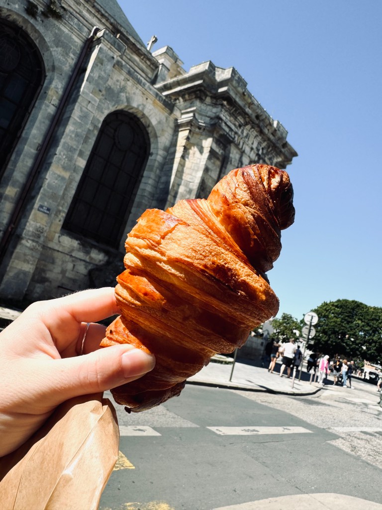 Hand holding croissant with old buildings in background in La Rochelle, France