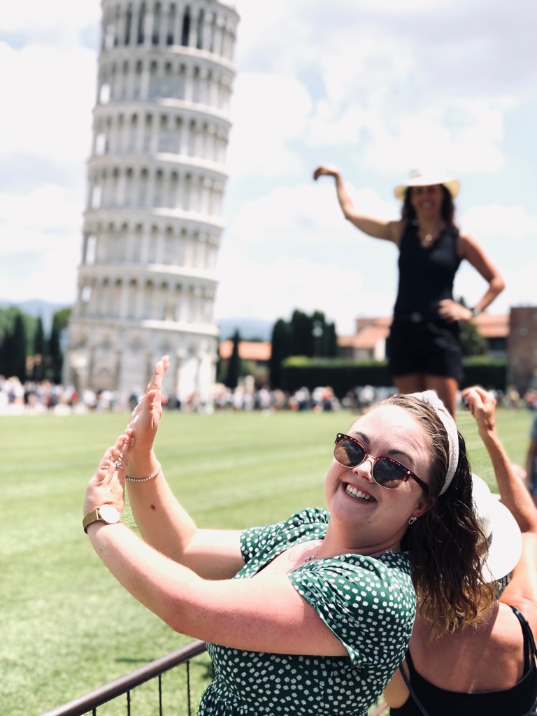 Girl posing in front of leaning tower of Pisa in Italy pretending to hold up tower but photo does not line up.