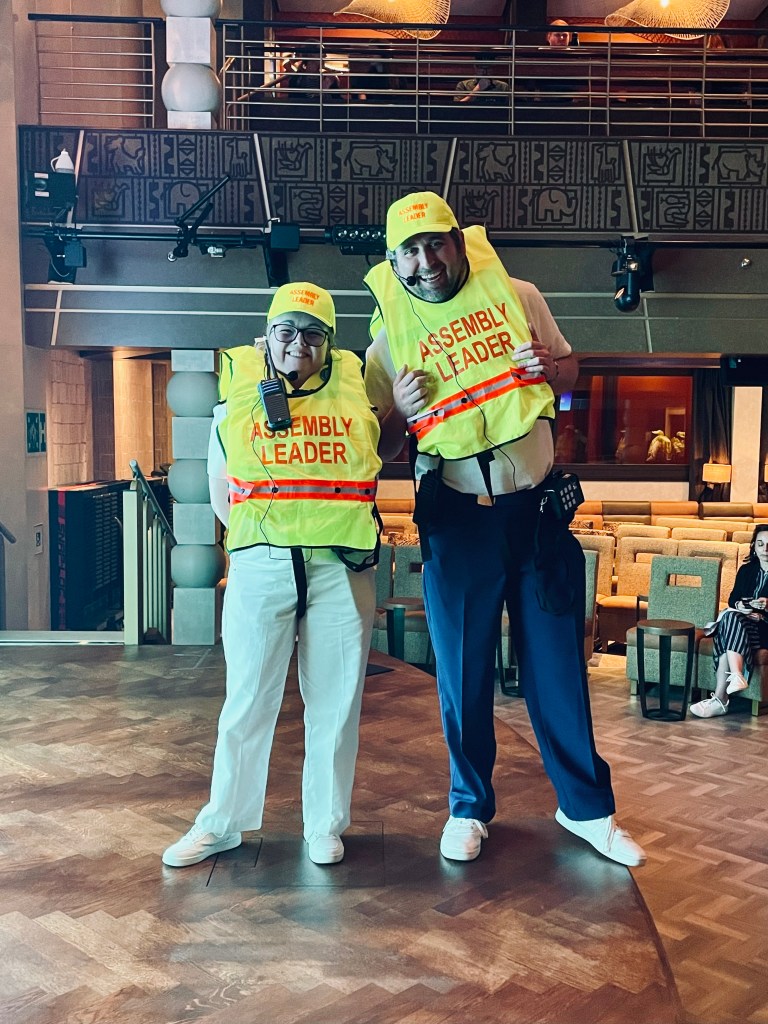 Two Disney Cruise Line crew members wearing fluro life jackets with "assembly leader" label