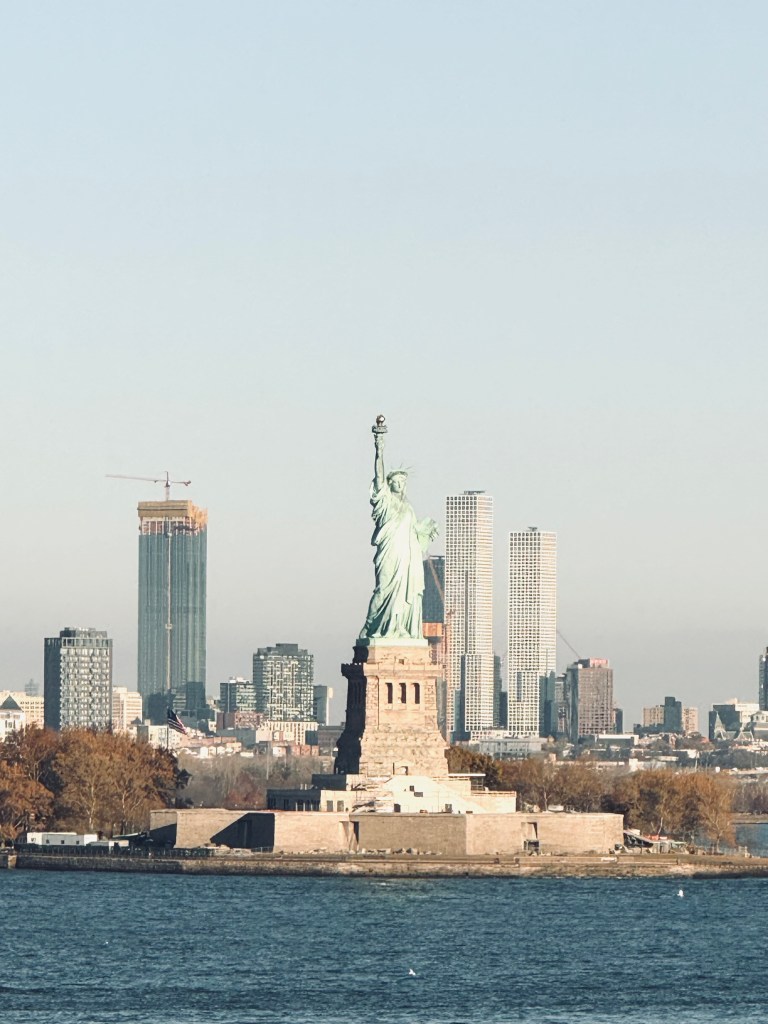 Statue of Liberty with city in background on a blue sky day