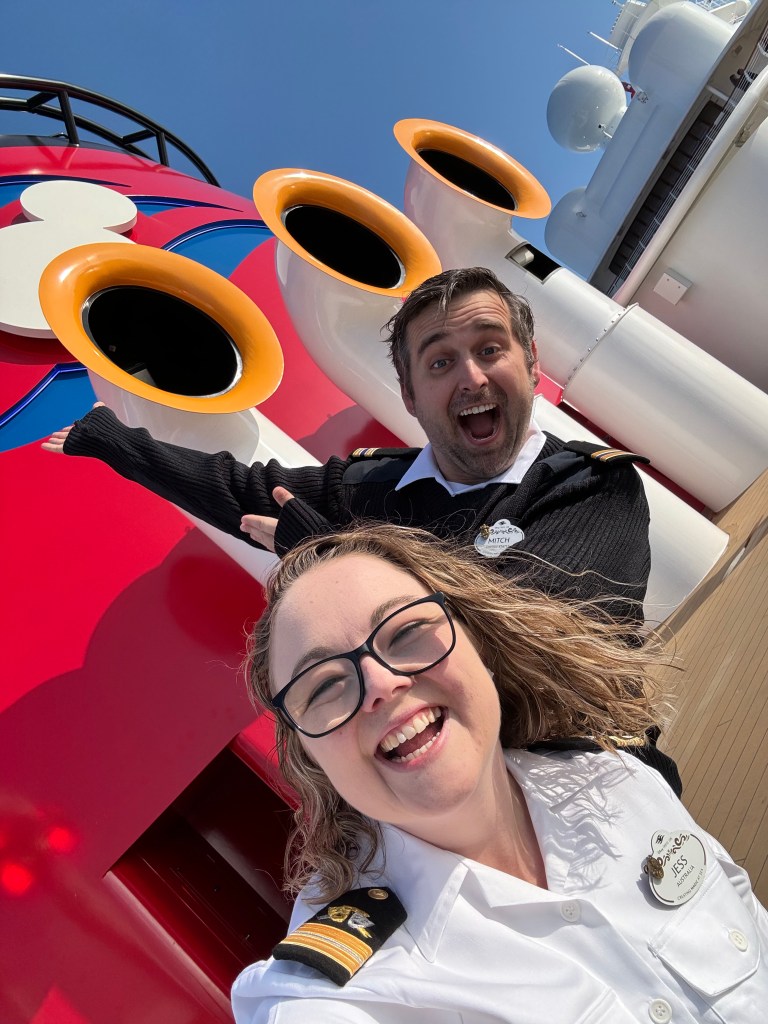 Two disney cruise line crew members taking selfie in front of Mickey Funnels