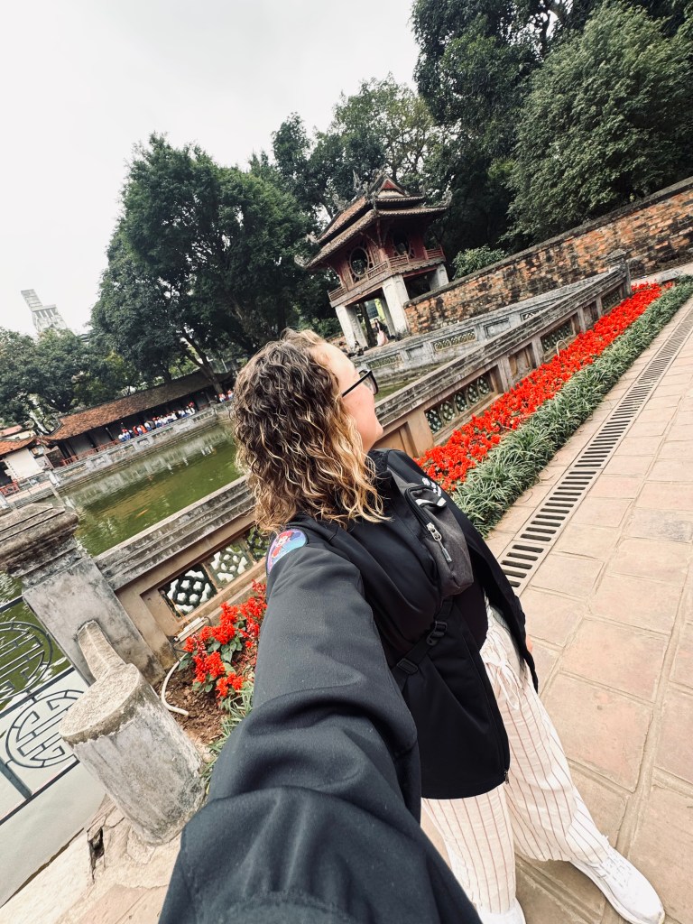 Girl taking selfie at Temple of Literature with red flowers and pond at Hanoi, Vietnam