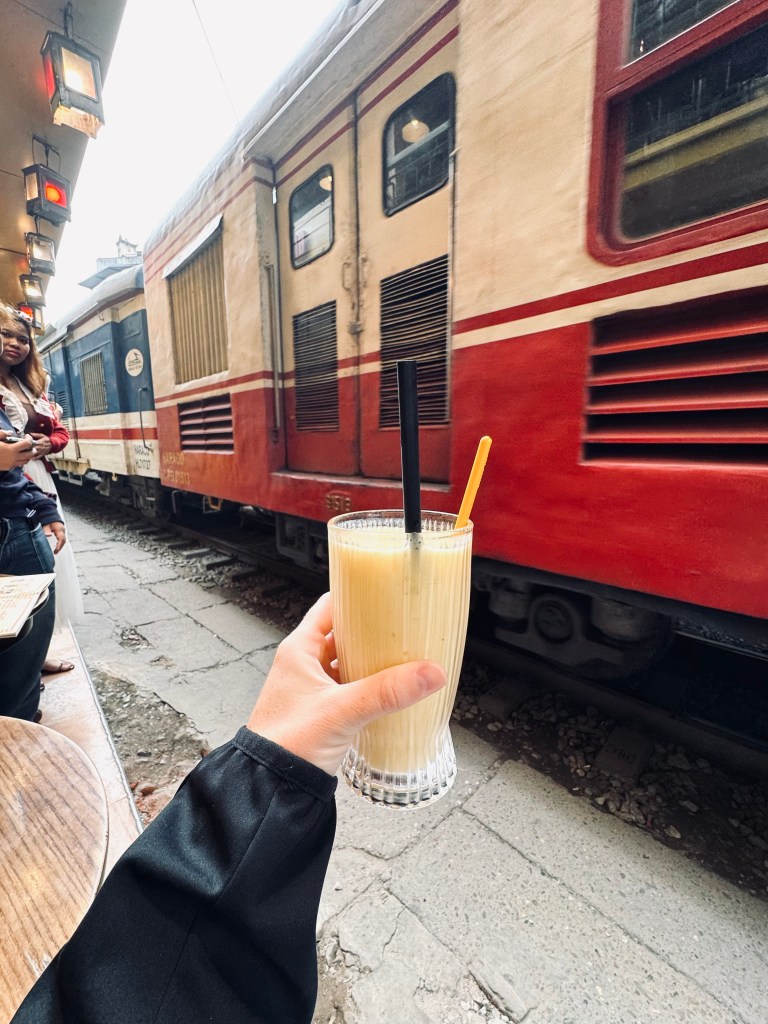 Hand holding smoothie in front of moving train on Train Street in Hanoi, Vietnam