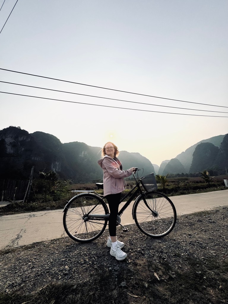 Girl smiling with bicycle at sunset with mountains in background in Ninh Binh, Vietnam