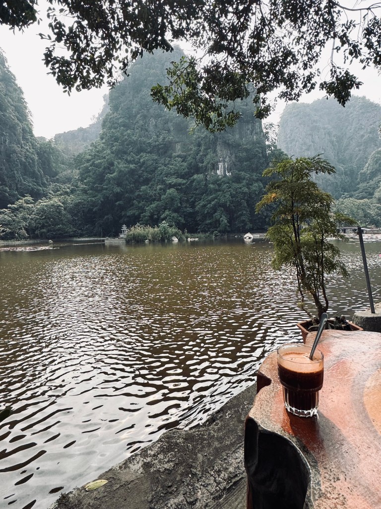 Coconut hot chocolate on a table in front of green river and cliffs in Ninh Binh, Vietnam