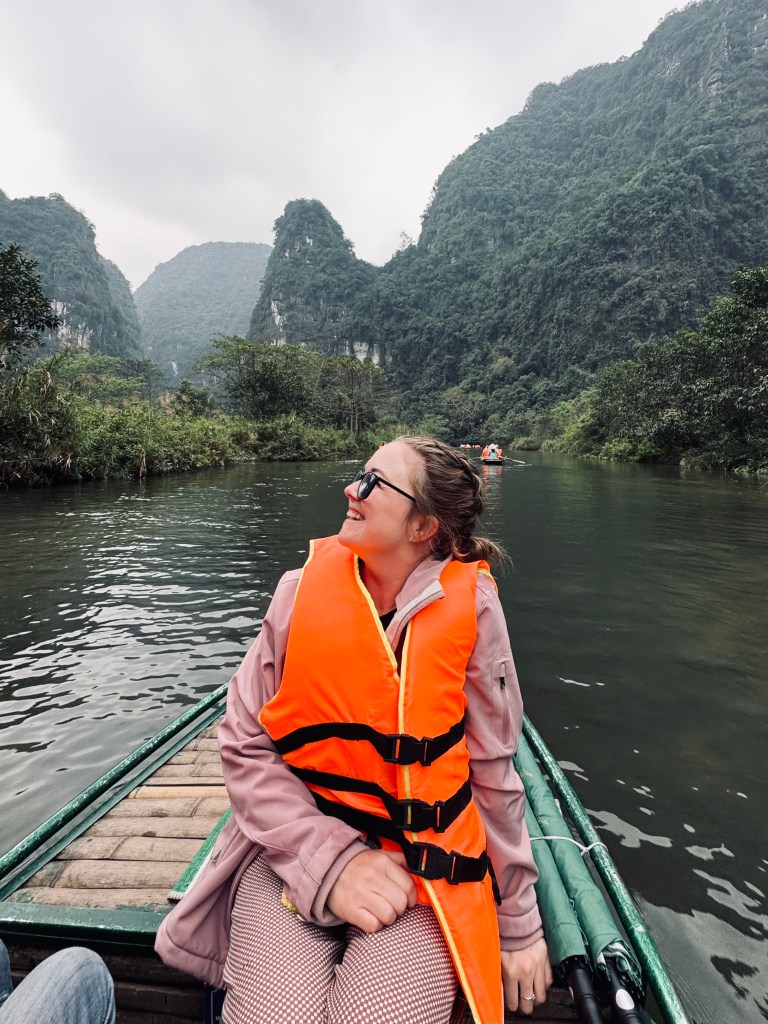 Girl smiling on Trang An boat ride with mountains in background in Ninh Binh, Vietnam