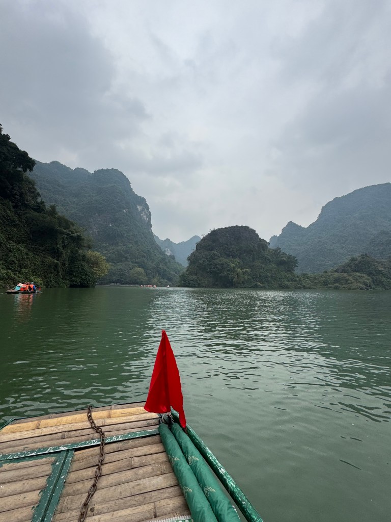Bamboo boat sailing on green water with limestone cliffs in distance at Trang An, Ninh Binh, Vietnam