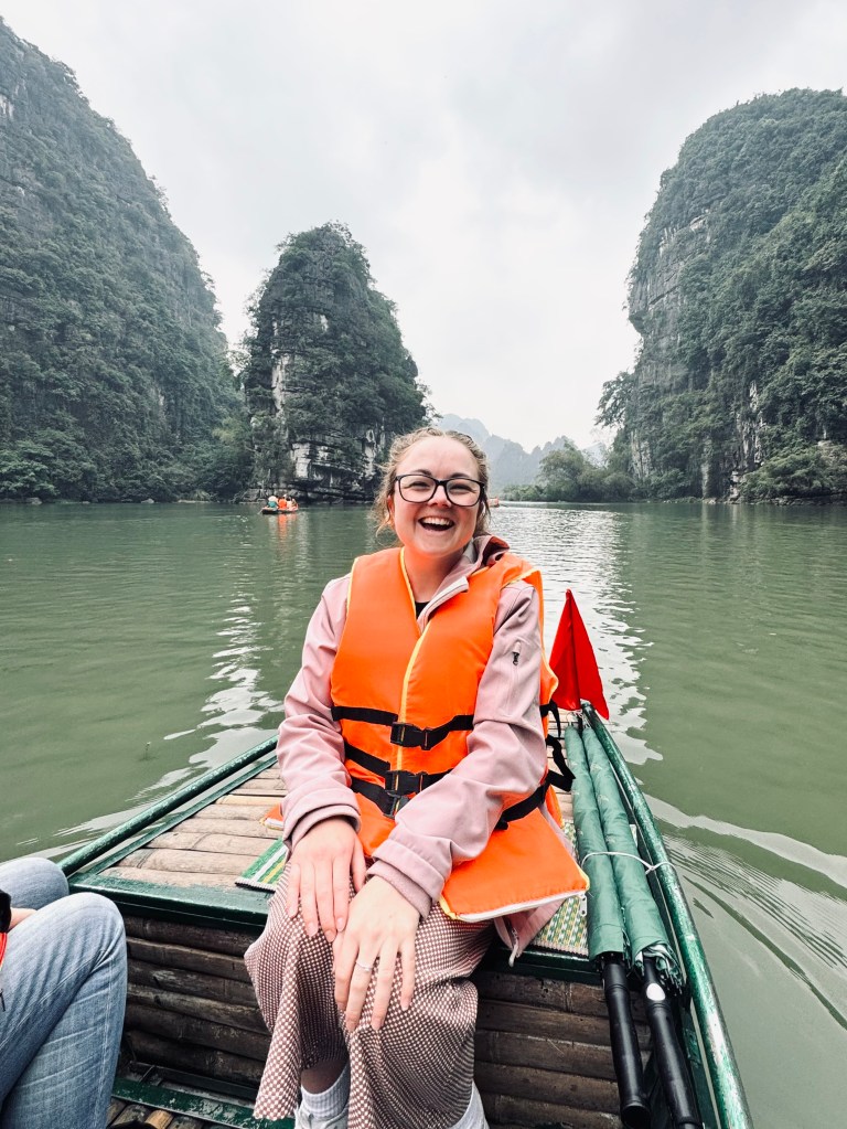 Girl sitting on boat on Trang An boat ride with mountains in background in Ninh Binh, Vietnam