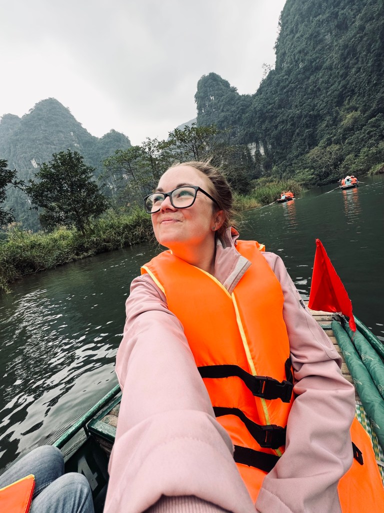 Girl taking selfie on Trang An boat ride with mountains in background in Ninh Binh, Vietnam
